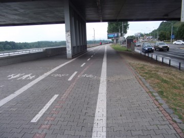 Priestor pre chodcov je rozdelený cyklotrasou na dve časti. Navrhujeme posun cyklotrasy vpravo, ku trávnatému pásu. Vhodná by bola aj náhrada zámkovej dlažby na cyklotrase hladším povrchom.